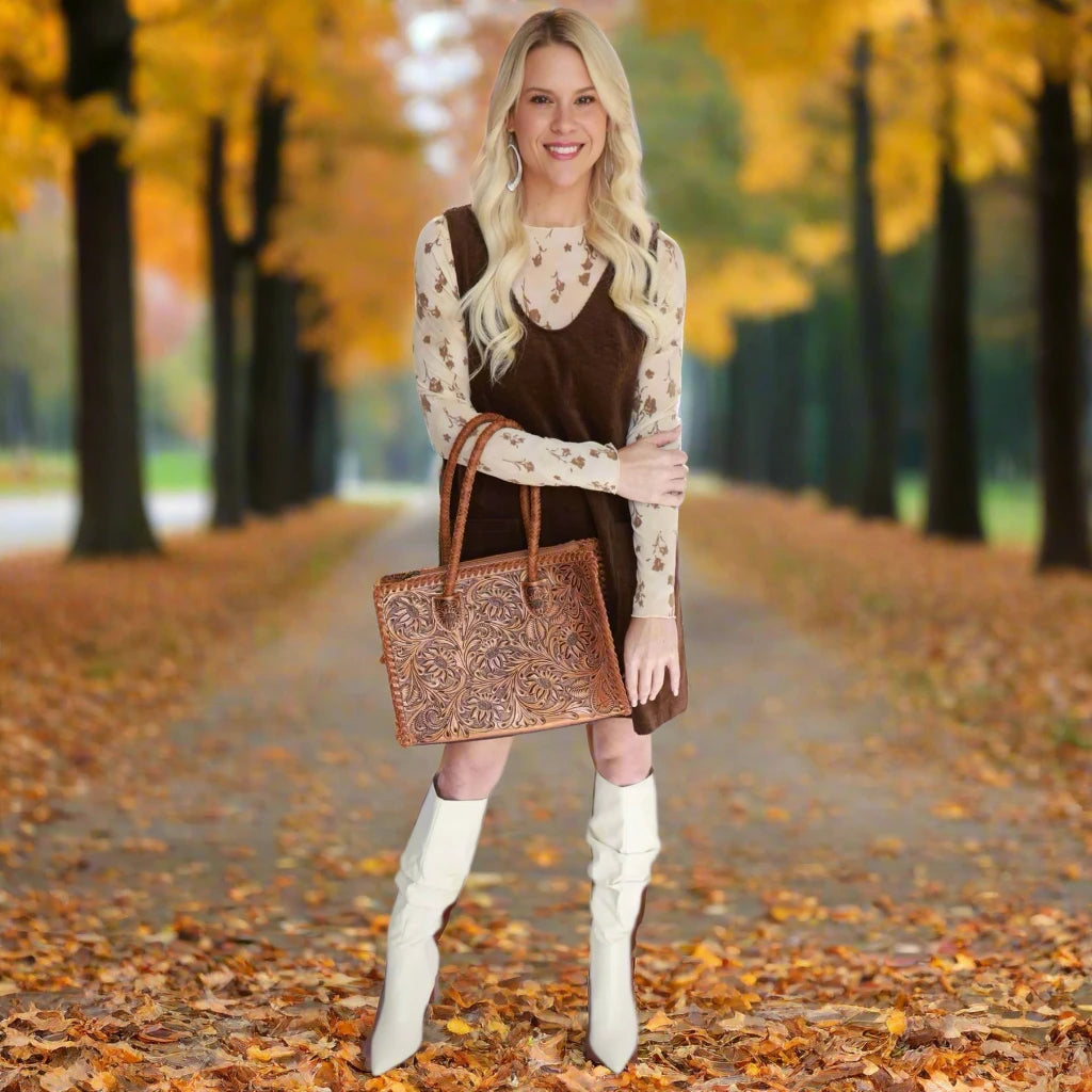 Woman wearing a brown dress with a floral top, white knee-high boots, and holding a patterned bag against a white background.