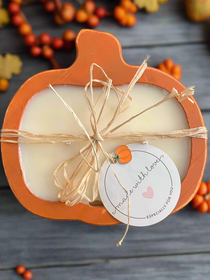 Candle in a pumpkin-shaped holder with twine and a label on a wooden surface