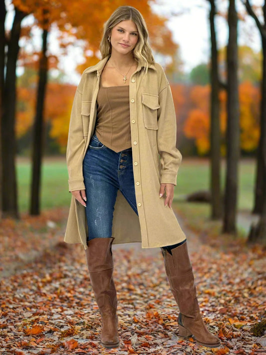 Woman wearing a beige trench coat, brown top, blue jeans, and brown knee-high boots on a white background