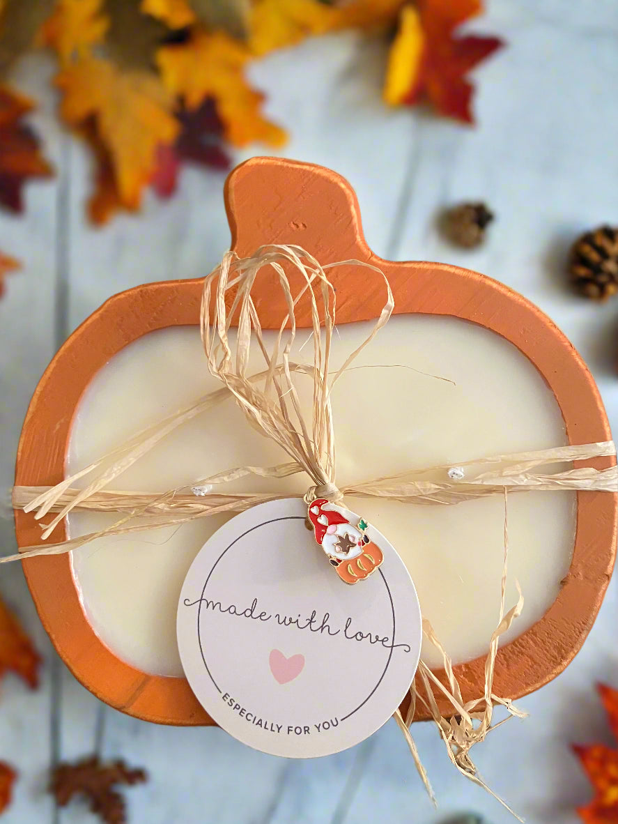 Candle in an orange holder with decorative string and a label on a wooden surface