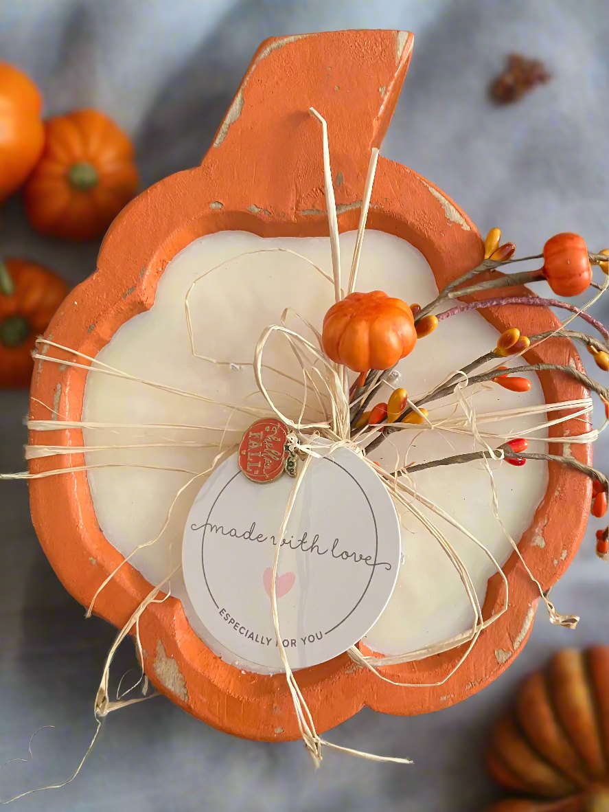 Decorative item with white candle, orange shell, and small orange flowers on a wooden surface.